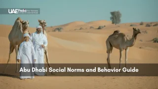 Emirati man and boy dressed in kanduras stand with camels against sweeping desert dunes.