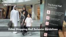 Family shopping in Dubai Mall beside behavior guideline sign.