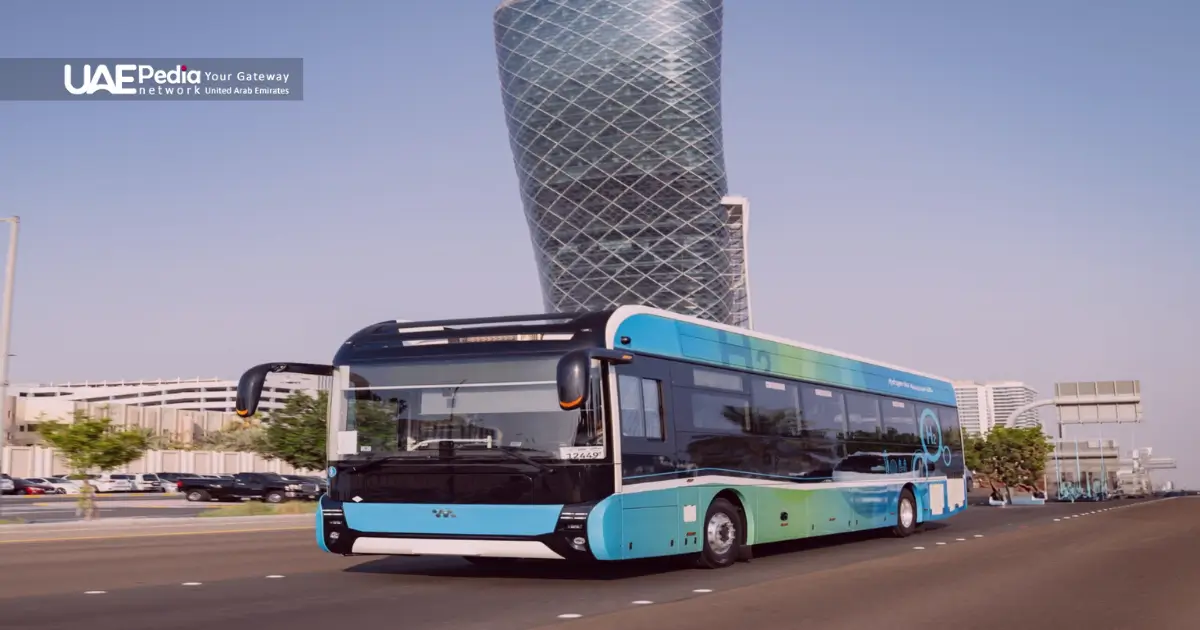 Electric city bus with blue-green livery driving past the iconic leaning Capital Gate building in Abu Dhabi.