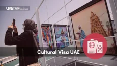Woman wearing a face mask and hijab takes smartphone photos of framed paintings at outdoor exhibit.