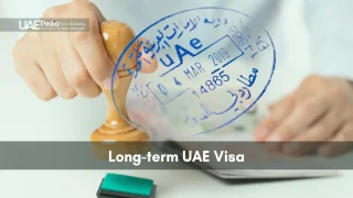 Hand pressing a wooden stamp to mark a passport with a blue UAE long-term visa imprint.
