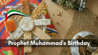 Assorted Middle Eastern confections on decorative plate with UAE flag and "Prophet Muhammad's Birthday" text.