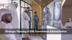 Group of Emirati dignitaries and uniformed officers gathered around monitors displaying government metrics