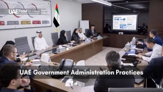 Group of men and women in formal attire at a conference table with UAE flag.