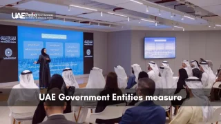 Woman presenting performance metrics to seated Emirati officials in a conference room.
