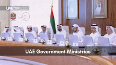 UAE ministers wearing white kanduras at a large conference table with UAE flag and portraits.