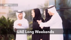A group of people in traditional attire discussing UAE Long Weekends outdoors.