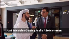 Man in traditional Emirati dress converses with a formally suited official in a contemporary public administration space