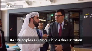 Man in traditional Emirati dress converses with a formally suited official in a contemporary public administration space