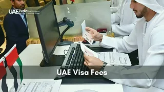 A man in Emirati dress examines passport and visa documents next to a computer.