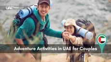 Smiling couple with backpacks climbing a rugged UAE trail by the water, UAEPedia logo visible