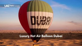 Hot air balloon with Dubai branding glides over sunlit dunes under clear sky.