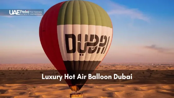 Hot air balloon with Dubai branding glides over sunlit dunes under clear sky.