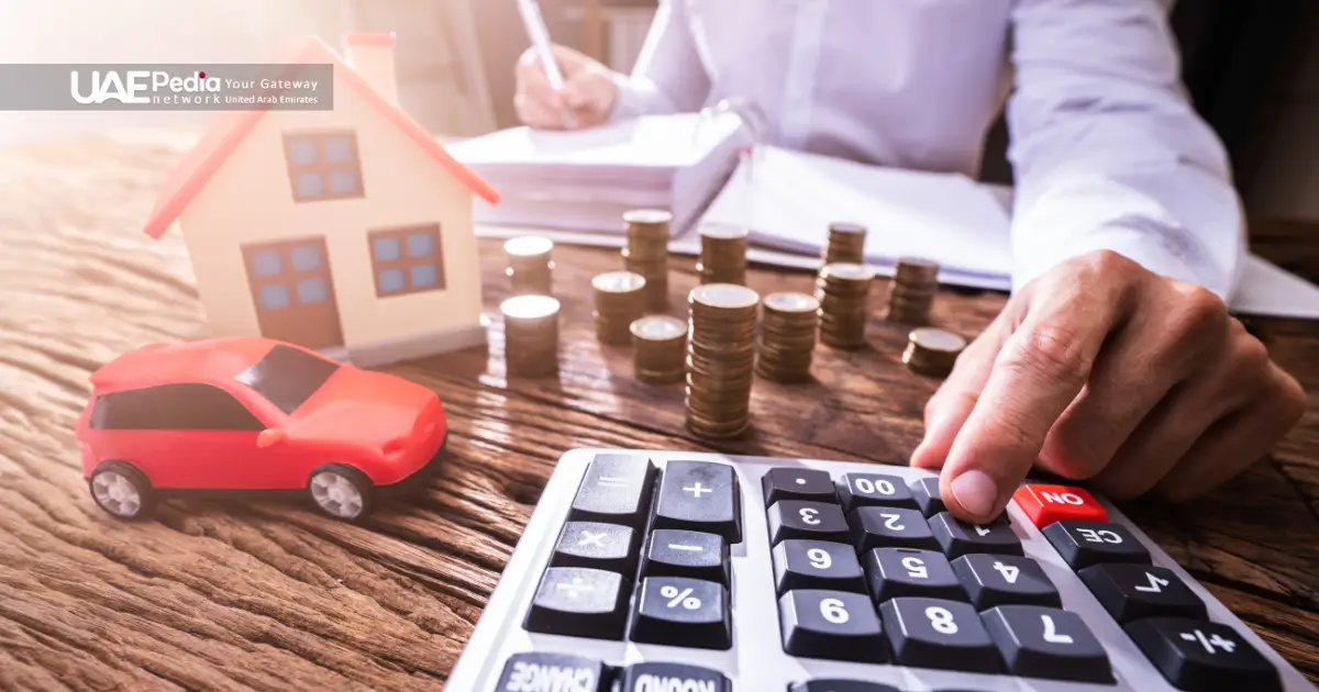 Person’s hand uses a calculator next to a small house model and coin stacks, illustrating rent calculations.