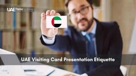 Man in suit holds a business card with a UAE flag icon against a blurred office backdrop.