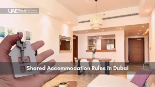 A hand holding a house-shaped key in front of a well-lit, modern apartment, illustrating shared accommodation rules.